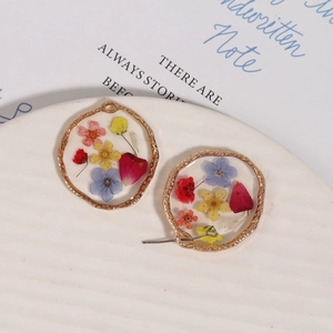 Macro shot of gold alloy resin charms with real dried flowers on white ceramic plate