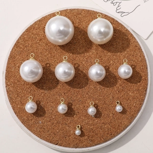 Various sizes of white imitation pearl pendants with gold rings on cork board