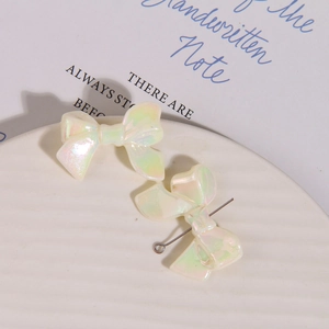 Macro view of iridescent white macaron bow jewelry charms on a ceramic plate for DIY crafts