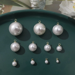 Macro view of white faux pearl charms in various sizes with golden metal hanging loops