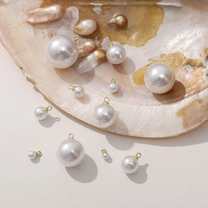 Macro view of multi-size round white pearl charms with gold metal loops for jewelry making