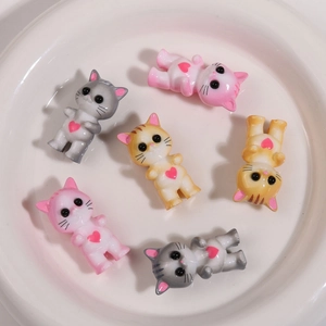 Dettaglio di 6 ciondoli gatto in resina colorata con cuori glitterati in una ciotola bianca
