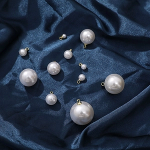 Close-up of assorted faux pearl pendants with gold loops on deep blue satin fabric