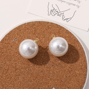 Close-up of two white faux pearl pendants with gold metal loops on a cork coaster