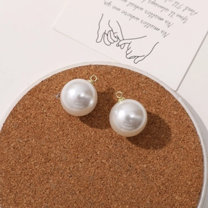 Macro shot of round cream white pearl pendants with gold rings on a cork coaster