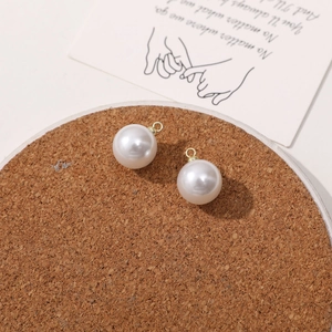Detail view of round white imitation pearl pendants with gold metal rings for DIY jewelry