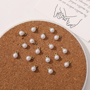 Detail of round faux pearl charms with golden loops for DIY jewelry on a cork pad