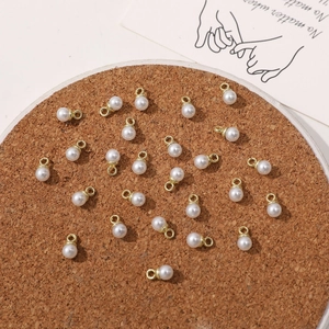 Close-up of DIY pearl pendants with gold rings for jewelry making on a cork surface