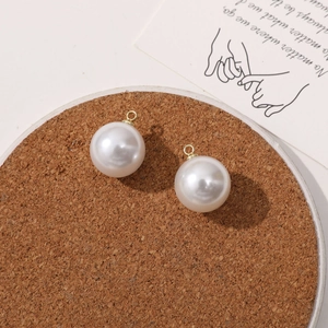 Close-up of DIY round imitation pearl pendants with golden metal loops on cork