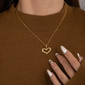 Gros plan d'un collier cœur doré à texture de lave sur un mannequin en pull marron
