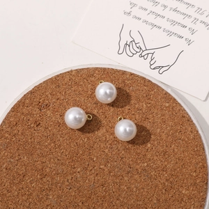 Close-up of three 10mm white faux pearl pendants with gold loops for DIY jewelry making