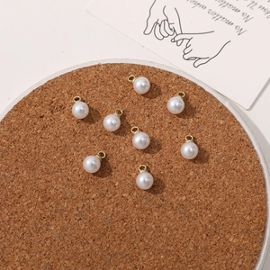 Flat lay of imitation pearl pendants with gold loops on a cork mat for DIY jewelry