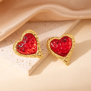 Detalle de pendientes en forma de corazón con piedra roja y acabado en oro martilleado