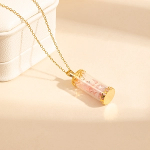 Detail of gold glass bottle necklace with pink natural stones on white jewelry case