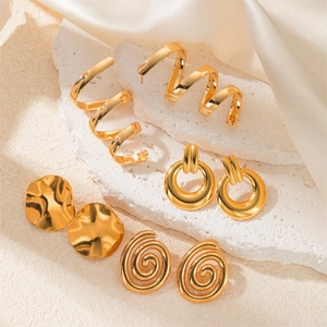 Macro view of gold plated wing and spiral earring set on elegant silk fabric background
