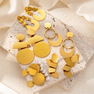 Detail view of gold-plated geometric wing earrings with white pearls on marble and silk