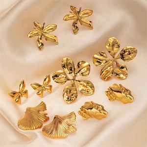 Close-up of gold plated stainless steel wing and leaf stud earrings on cream satin fabric