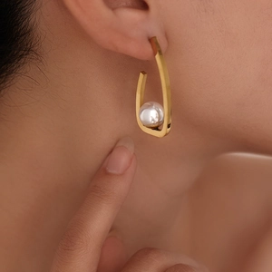 Close-up of gold U-shaped stainless steel earring with a white pearl on female model