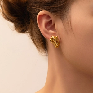 Close-up of golden geometric earrings with lava texture on female model's ear