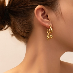 Close-up of elegant gold fluid-style earrings with polished finish on model's ear