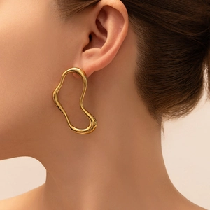 Macro side view of large wavy golden hoop earring with polished 18K finish on ear