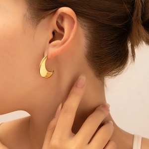 Close-up of a model wearing minimalist thick crescent 18K gold plated hoop earrings