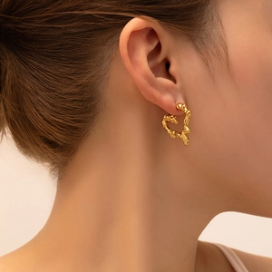 Close-up of golden heart earrings with liquid lava texture worn by a female model