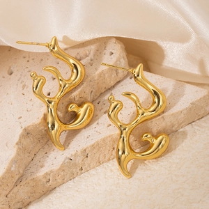 Detailed close-up of golden flame-shaped titanium earrings on silk fabric background