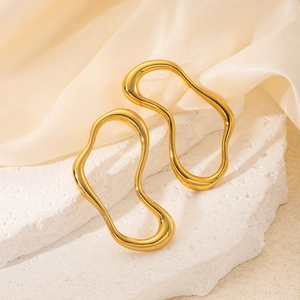 Close-up of golden wavy hoop earrings with a polished metallic finish on white stone