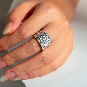Macro shot of silver wide band ring with irregular hammered texture and molten metal finish