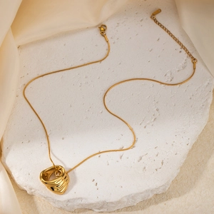 Detailed close-up of golden irregular block pendant on snake chain over white marble