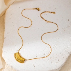 Detail of gold snake chain necklace featuring a curved textured tube pendant on stone