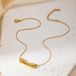 Detail of gold snake chain with minimalist curved bar pendant on a textured white stone