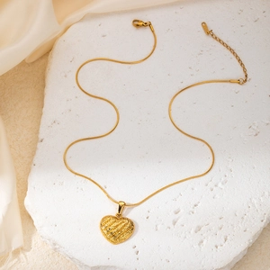 Detailed view of a golden heart pendant necklace with rock texture on white stone