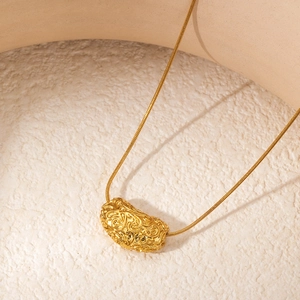 Detailed macro shot of gold bar necklace with intricate organic relief pendant on a beige surface