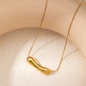 Close-up of golden teardrop pendant on a sleek snake chain over beige stone surface