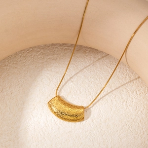 Detail of gold snake chain necklace with a textured lava rock style curved pendant