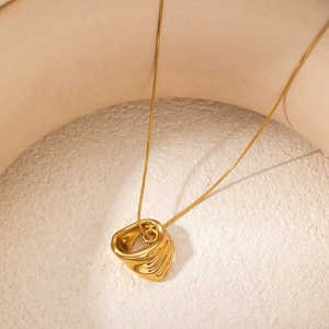 Close-up of golden necklace with irregular ripple ring pendant on sleek snake chain