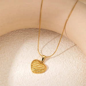 Macro detail of a golden heart pendant with a hammered texture on a snake chain