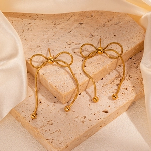 Dettaglio di orecchini a fiocco dorato con lunghe nappe e sfere metalliche eleganti