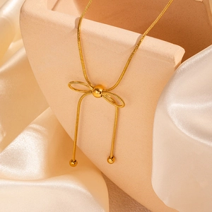Dettaglio di una collana con ciondolo a fiocco dorato e perle su tessuto di raso
