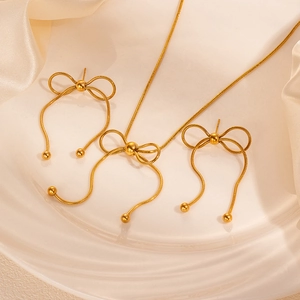 Macro di set gioielli con fiocco dorato e nappe su elegante sfondo di seta bianca