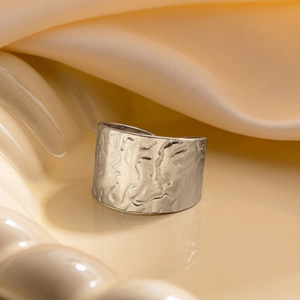 Détail macro d'une bague large argentée avec texture martelée irrégulière sur céramique