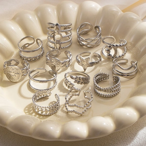 Dettaglio di anelli multistrato argento con stelle e forme geometriche su piatto ceramica