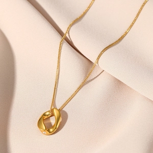 Macro shot of 18K gold plated twisted ring pendant with a sparkling zircon on pink fabric