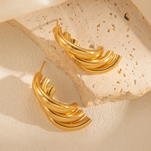 Close-up of chunky triple-layered gold hoop earrings on textured stone and white silk