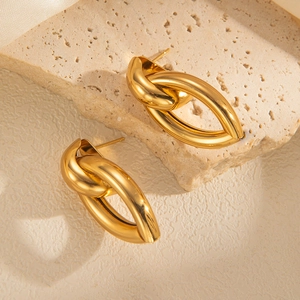 Close-up of chunky gold knot earrings displayed on a natural beige stone backdrop