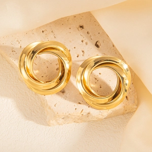 Detail of three intertwined golden circles stud earrings on a textured beige stone background