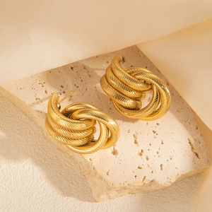 Detailed shot of vintage gold twisted rope earrings on a beige stone and silk background
