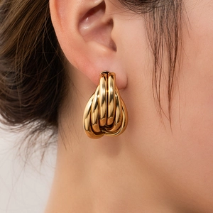 Close-up of golden multi-layered intertwined hoop earrings worn by a female model